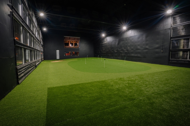 Golfa zāle ar ripināšanas grīnu, melnām sienām un griestu apgaismojumu
